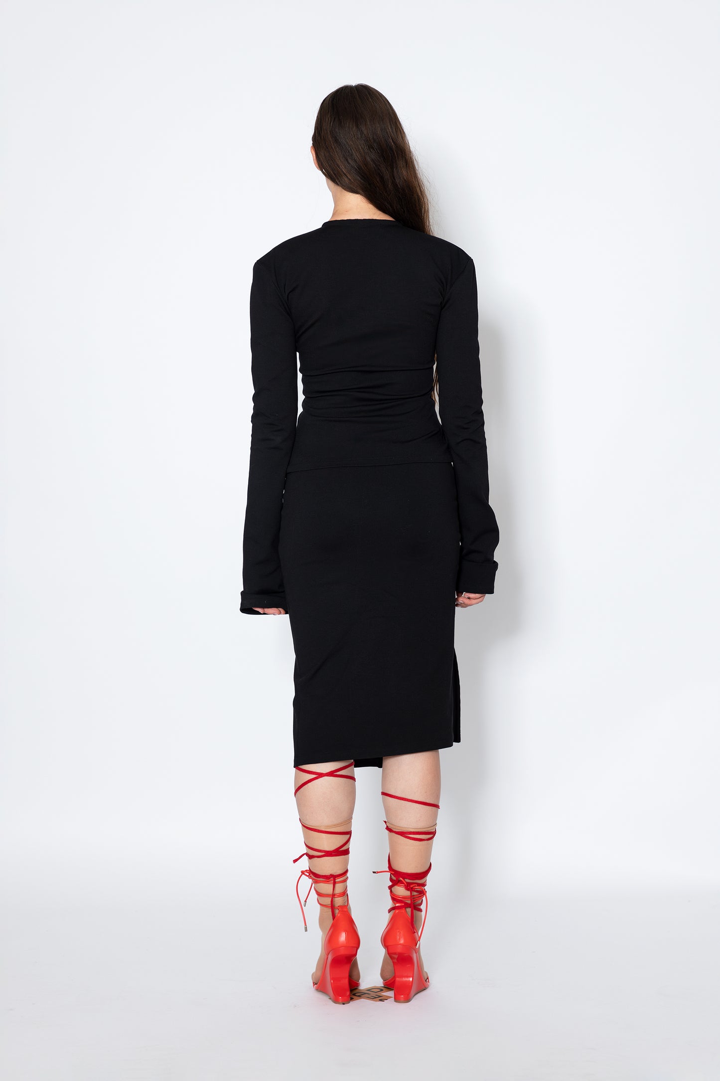 Model shows Jade Cropper Black Midi Skirt With Hook-Eye back view with fitted cut ruched detail slit hem and long sleeves