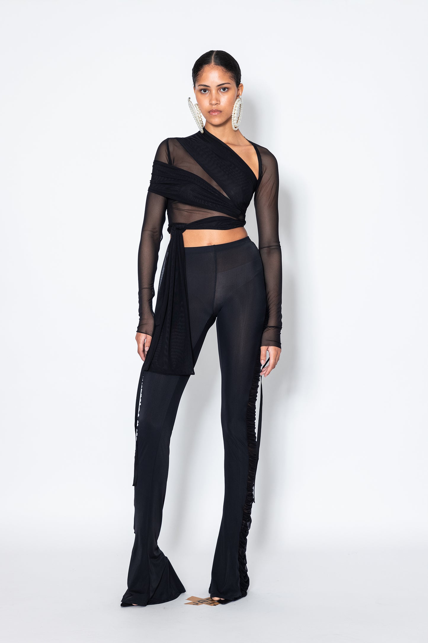 Model wears Jade Cropper Black Semi-Sheer Ruched Pants front view with asymmetrical hem and mesh wrap design long sleeves