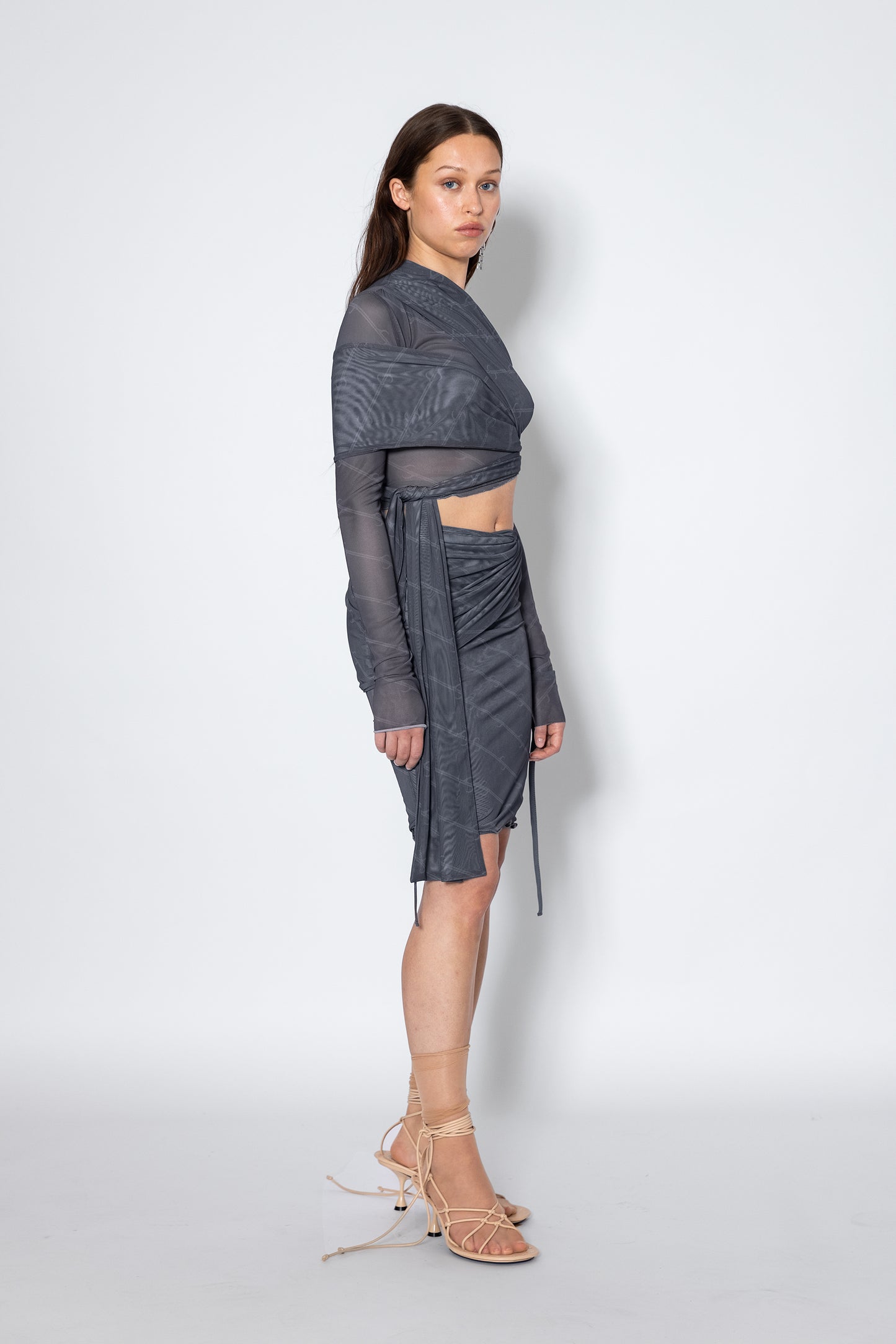 Model wears Jade Cropper gray mesh fabric garment with asymmetrical hem long sleeves and logo detailing side view