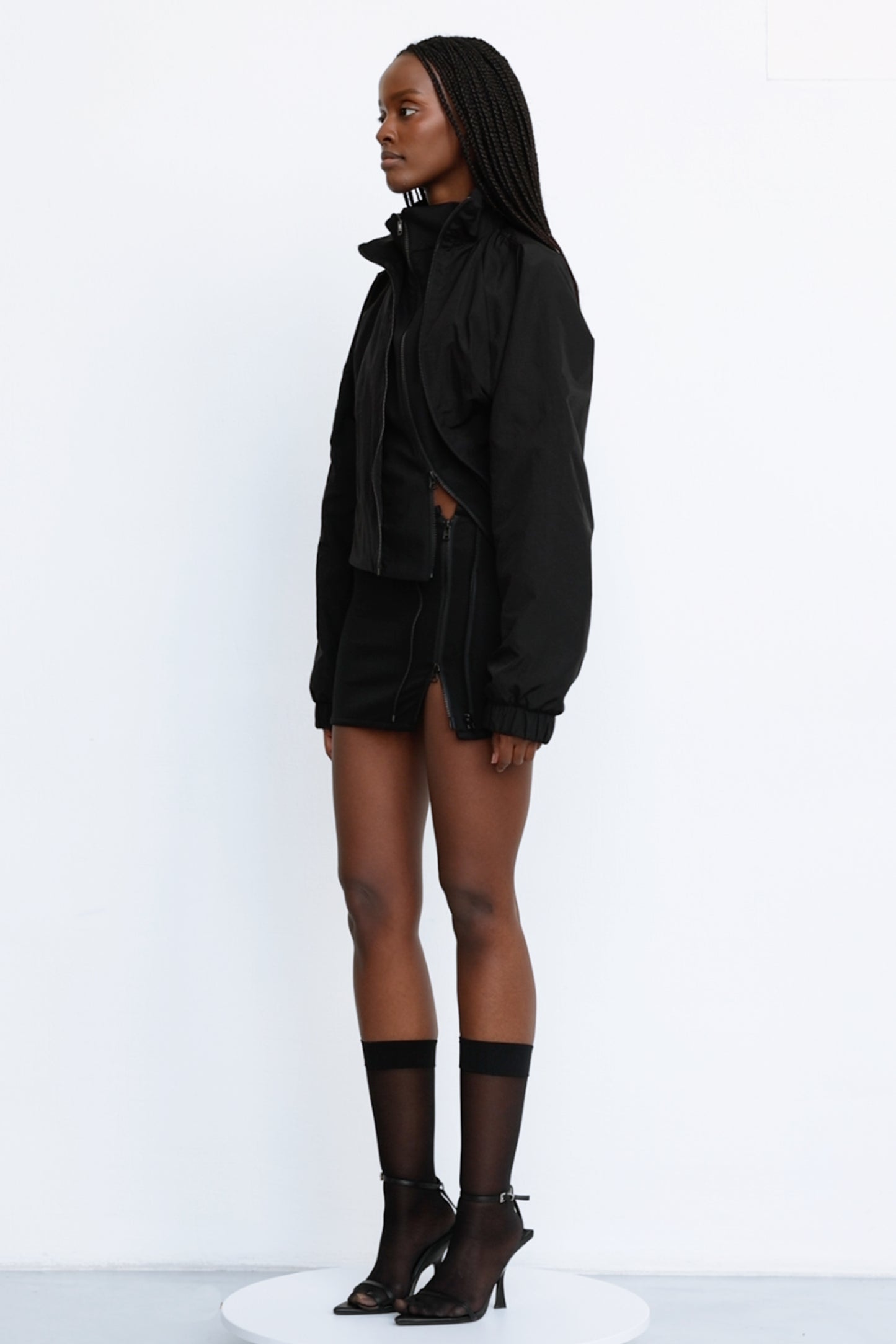 Model wears Jade Cropper Asymmetric Layered Jacket in black side view with cropped cut, padded shoulders, and zip closure