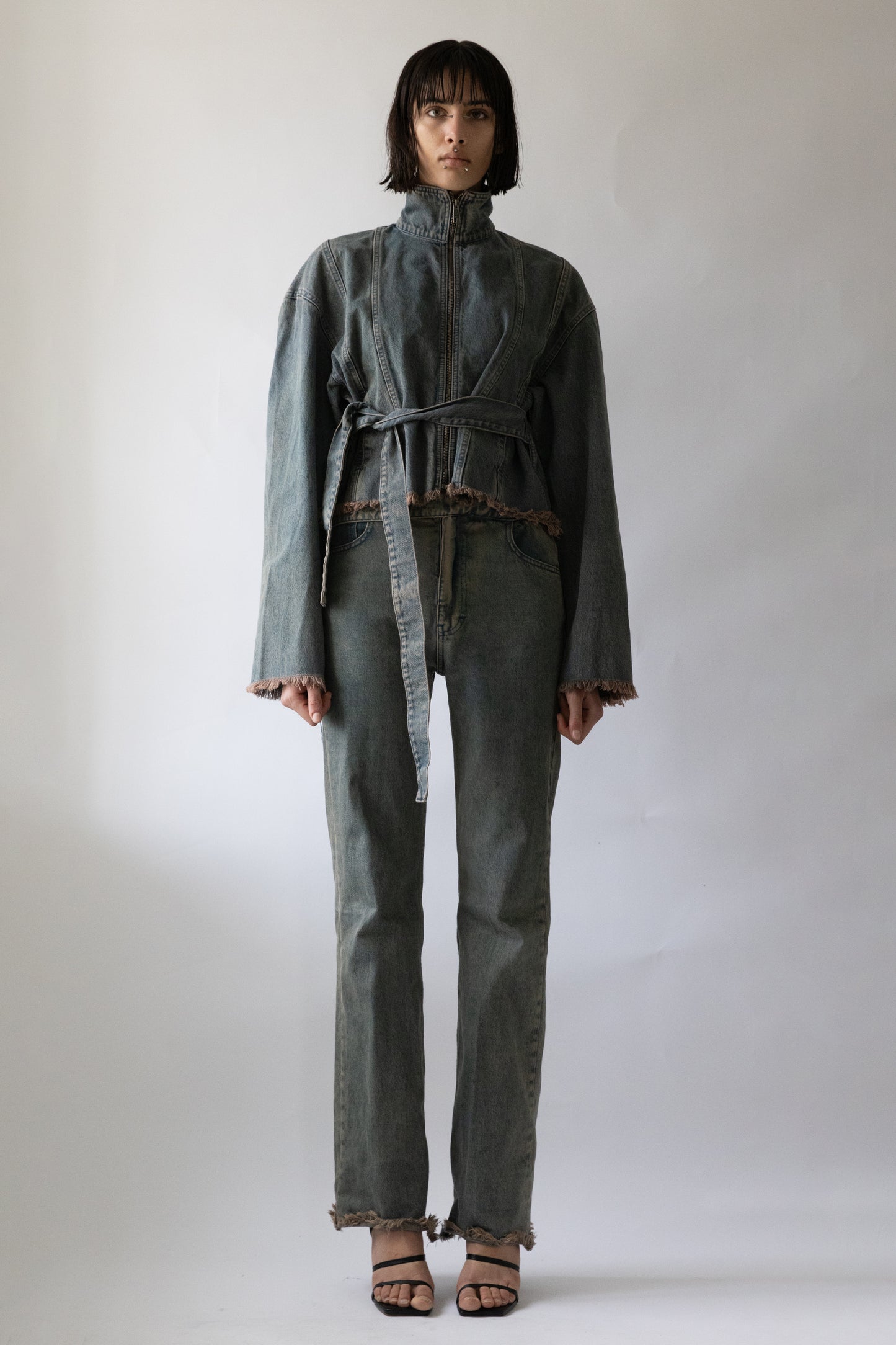 Model wearing Jade Cropper gray garment with belted waist, zip closure, long sleeves, and frayed hem front view