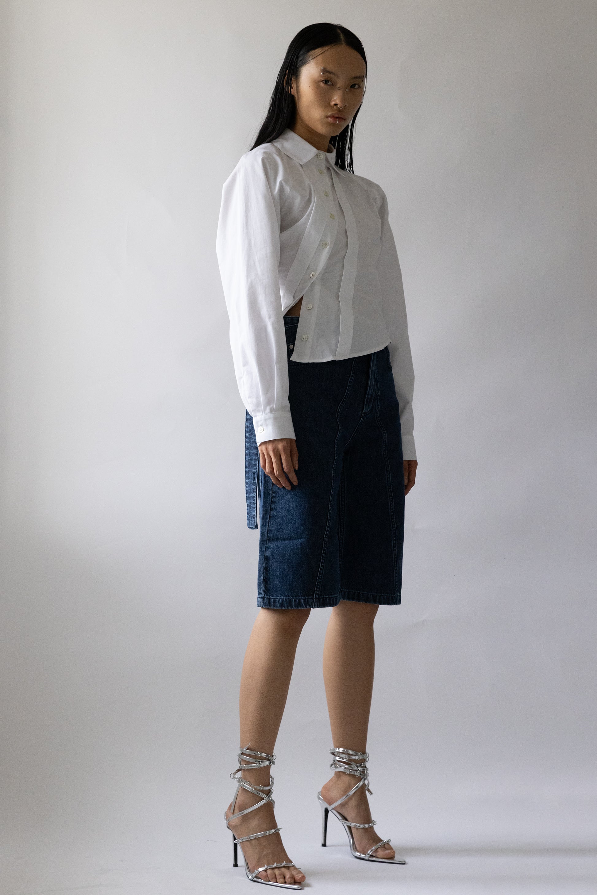 model side profile wears above-knee cut blue denim five-pocket garment with raw hem by Jade Cropper