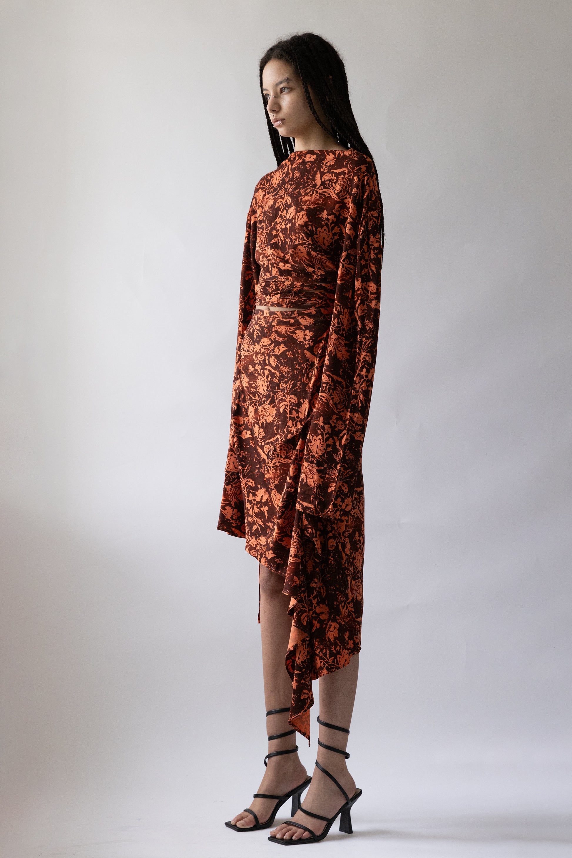 Side view of Jade Cropper Draped Asymmetric Wrap Skirt in orange featuring asymmetric hem long sleeves floral stretch fabric on model