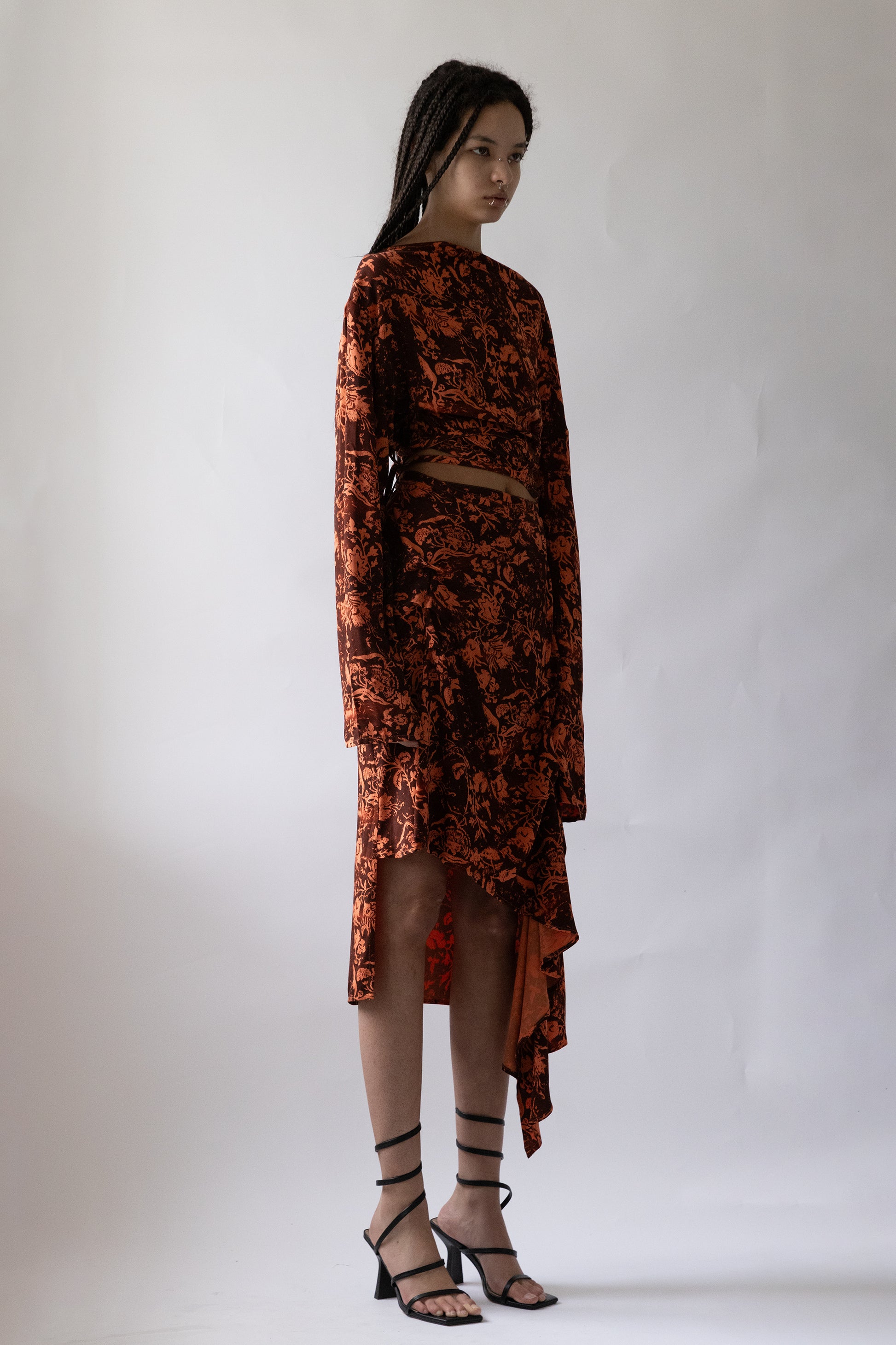 Orange patterned fabric Draped Asymmetric Wrap Skirt by Jade Cropper shown from side with cropped hem and long sleeve on model