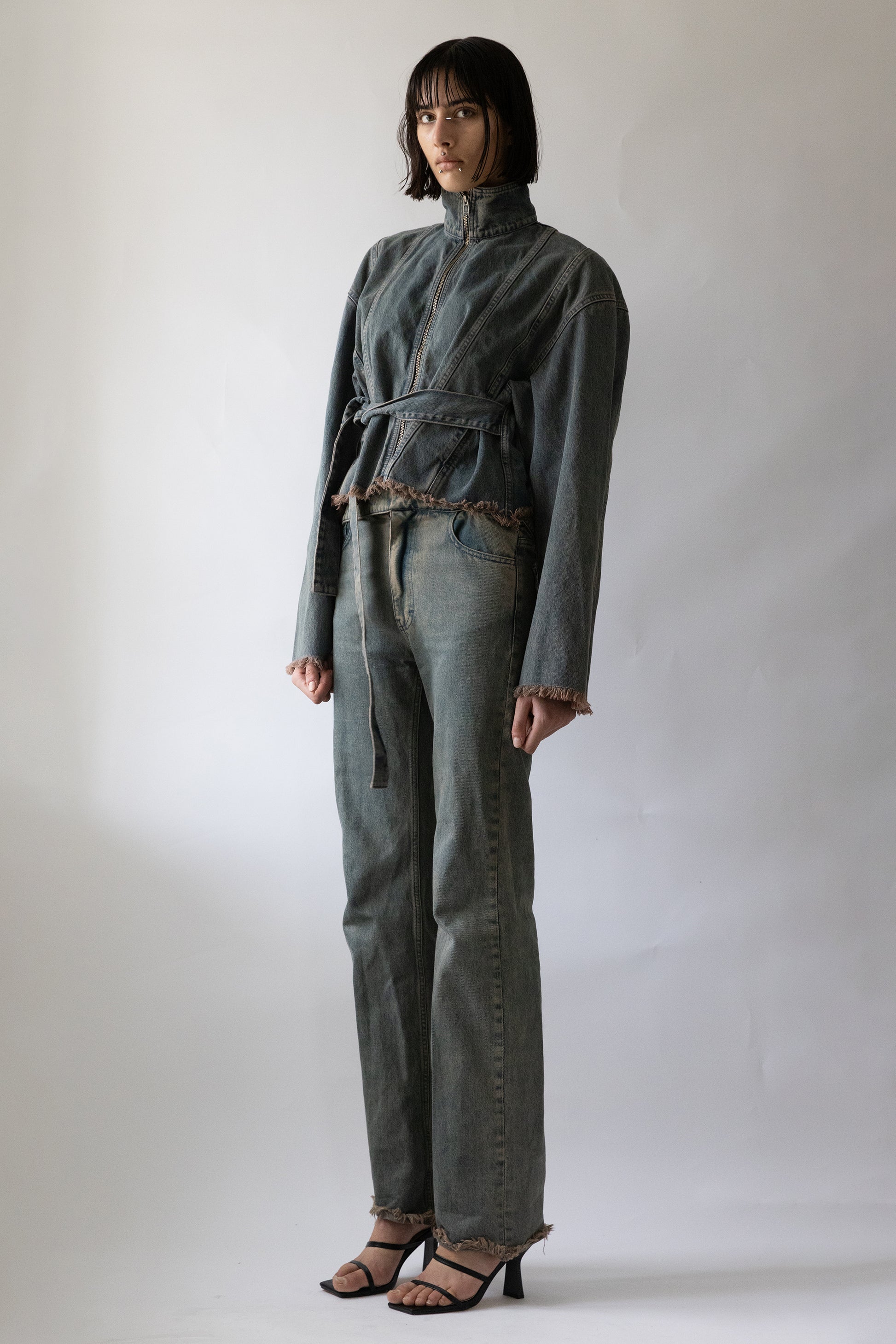 Model wearing Jade Cropper gray cropped garment with zipper closure, belted waist, and frayed hem front view