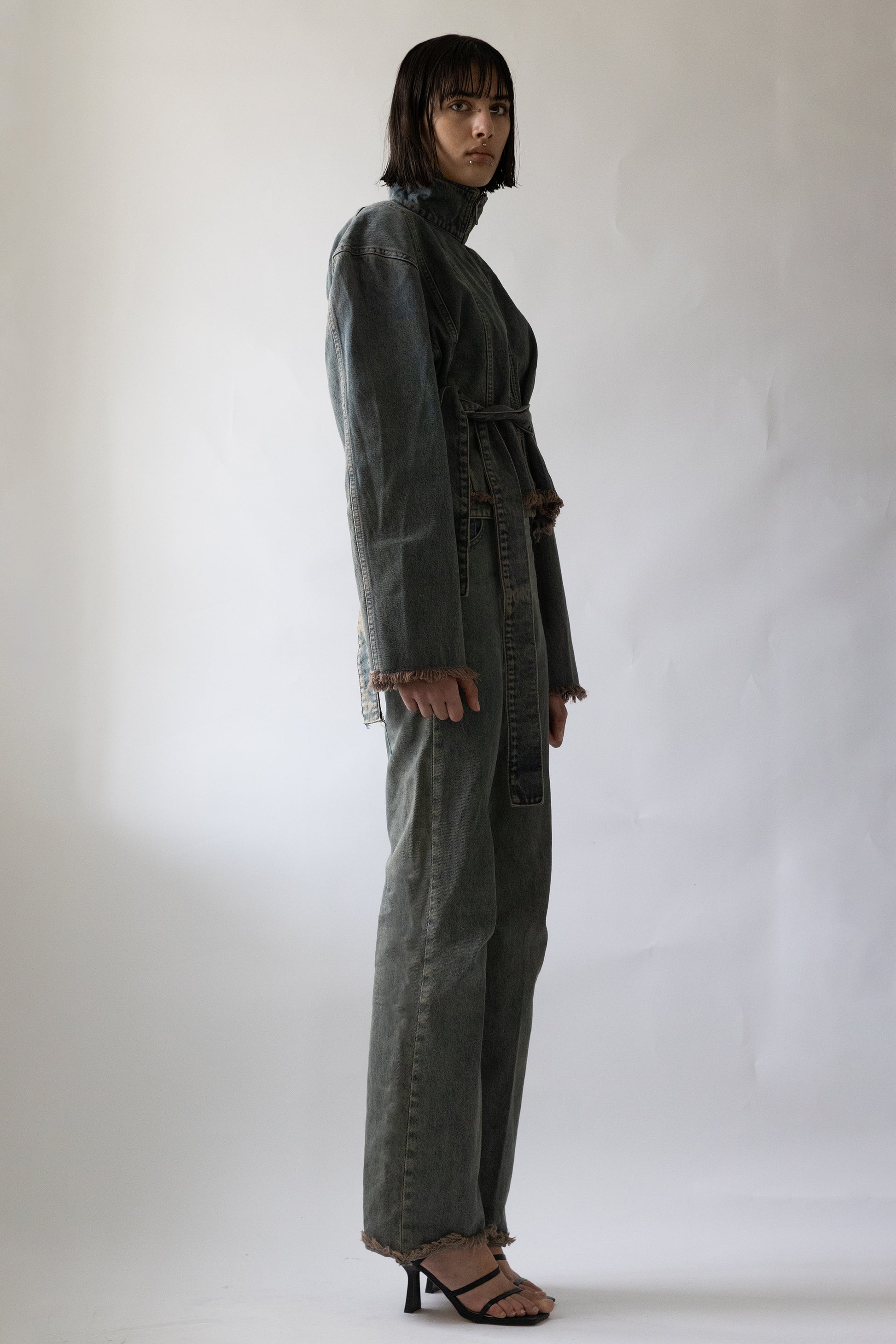 Model wearing Jade Cropper gray garment with belted waist, collar, long sleeves, and frayed hem side view