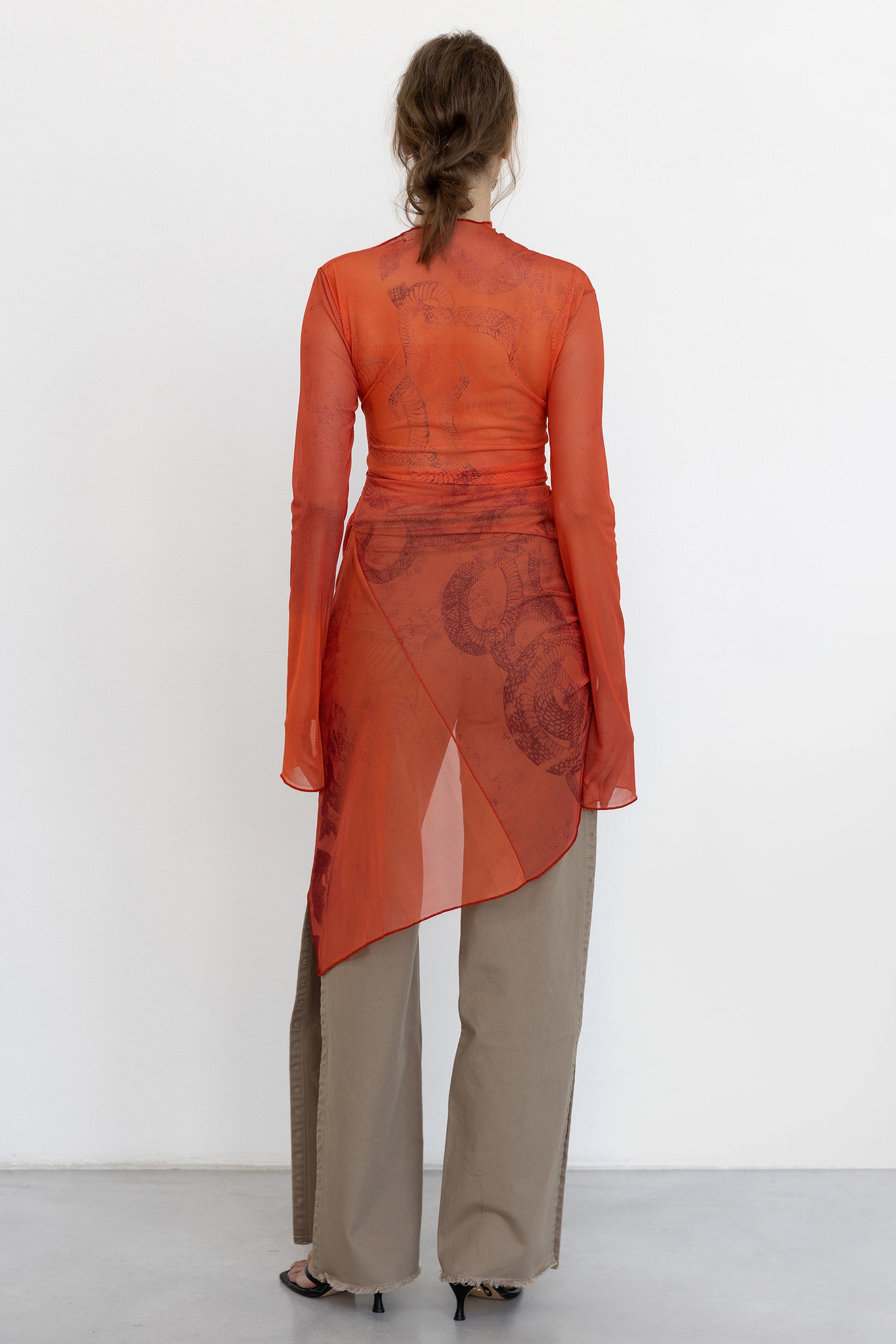 Model shows back view of Jade Cropper Draped Twisted Dress in red showcasing sheer draped fabric long sleeves and asymmetric hem