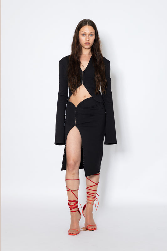 Model wears Jade Cropper Black Midi Skirt With Hook-Eye front view with high slit cut-out detail and zip closure long sleeves