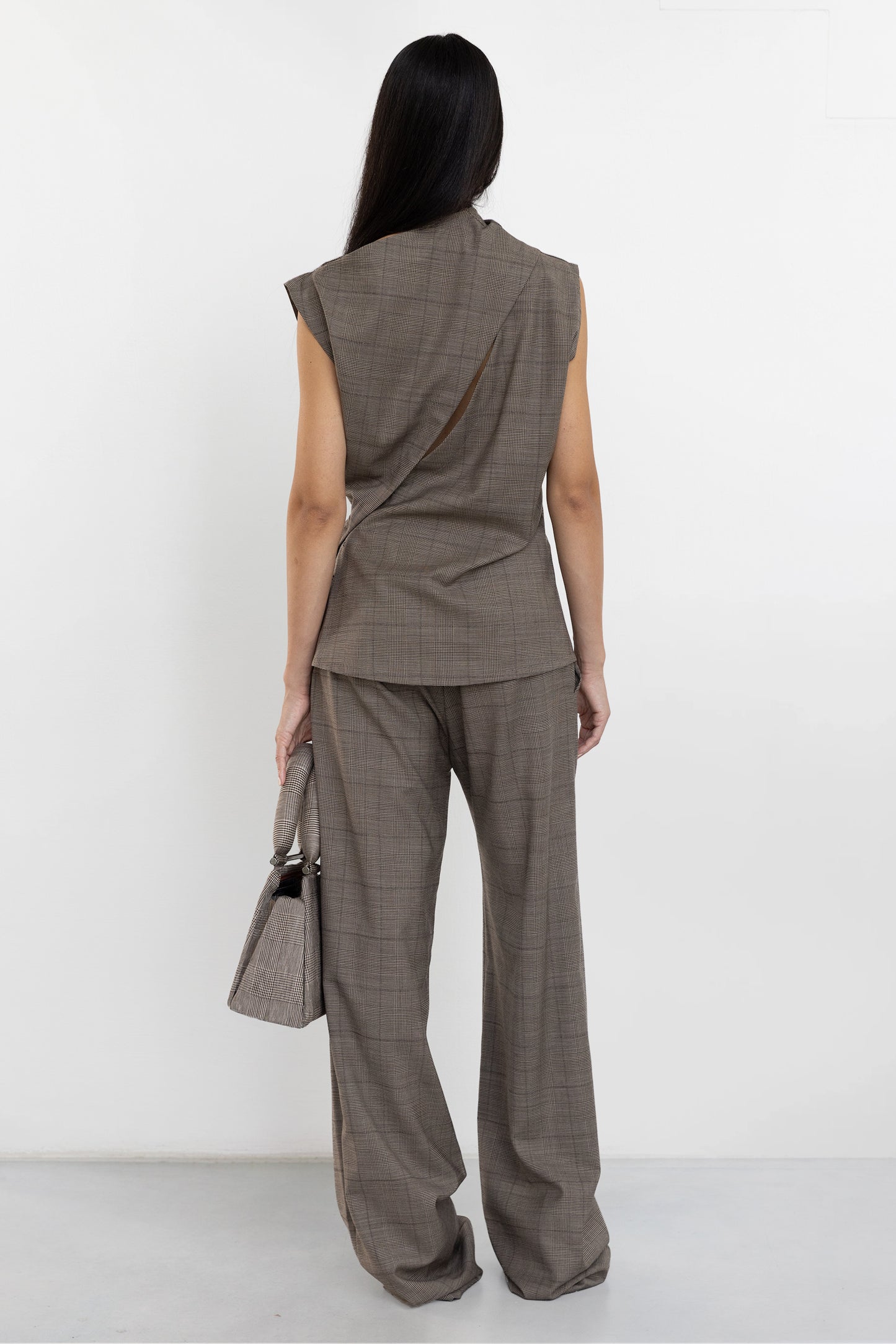 Back view of Jade Cropper asymmetric suit top with open back in brown plaid showing curved legs and precise tailoring
