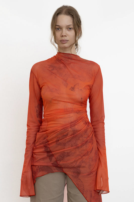 Model wears Jade Cropper Draped Twisted Dress front view in red with sheer fabric long sleeves and asymmetrical hem draped detail
